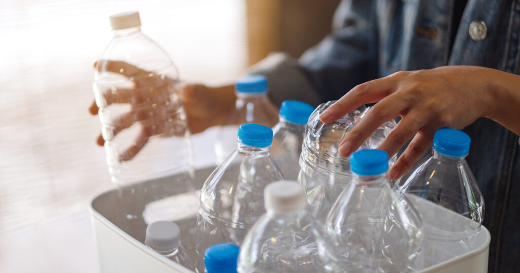 A woman collecting and separating recyclable garbage plastic bottles into a trash bin at home